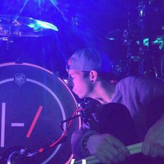 a man holding a large drum in front of a blue and purple light with his face close to the drumset