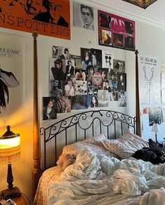 an unmade bed in a bedroom with posters on the wall above it and a lamp next to it