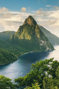 an island in the middle of a body of water surrounded by trees and mountains with clouds