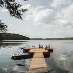 two boats are docked at the end of a wooden dock on a lake with clouds in the sky