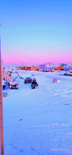 cars are parked in the snow near some houses and buildings at sunset or dawn on a cold winter day