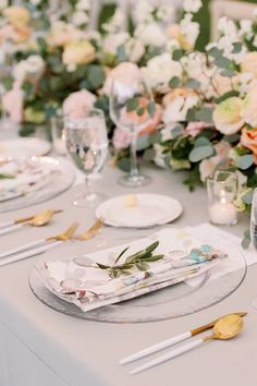 the table is set with white and gold place settings, silverware, and floral centerpieces