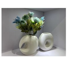 two white vases with flowers in them sitting on a counter top next to each other