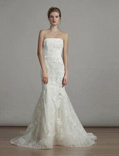 a woman in a strapless wedding dress standing on a wooden floor with her hands behind her back