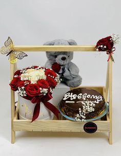 a teddy bear sitting on top of a wooden shelf next to a cake and flowers