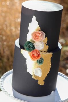 a black and gold wedding cake with flowers on it