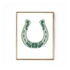 a green horseshoe with flowers on it is mounted in a gold frame against a white wall