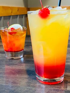 two cocktails sitting on top of a wooden table next to each other, one orange and the other red