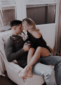 a man and woman sitting on top of a white chair with their feet in each other's lap