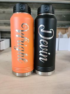 two orange and black water bottles sitting on top of a wooden table next to each other