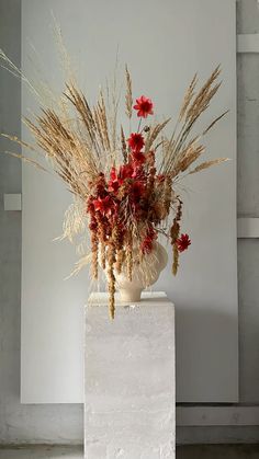 a vase filled with lots of flowers sitting on top of a white pedestal next to a wall