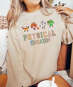 a woman sitting on the floor wearing a sweatshirt that says physical education with cartoon characters