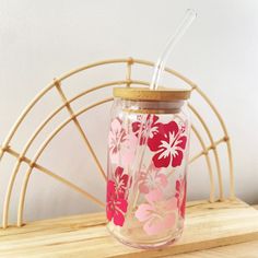 a pink and red flowered mason jar with straws on a wooden table next to a bamboo chair