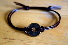 a brown leather bracelet with a coin on the clasp and a cord around it, sitting on a wooden surface