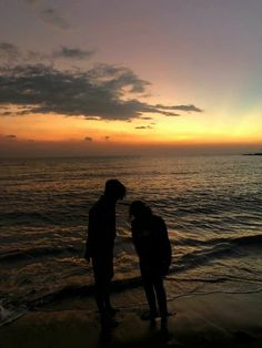 two people are standing on the beach and facing each other as the sun is setting