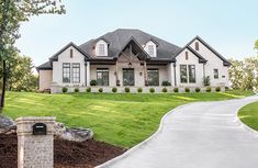 a large white house sitting in the middle of a lush green field next to a driveway