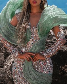 a woman in a green dress is standing on the rocks with her arms around her body