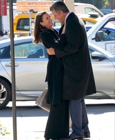 a man and woman standing next to each other on a sidewalk in front of parked cars