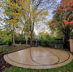 an outdoor basketball court surrounded by trees and bushes with a man standing in the middle