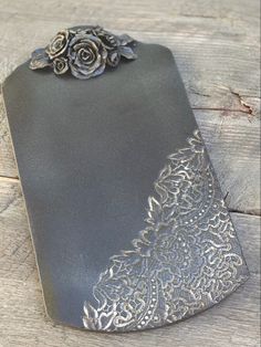 this is an image of a black and silver flower on a piece of metal with wood in the background