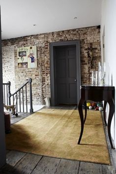 a room with a wooden floor and brick wall behind the door to another room that has an area rug on it