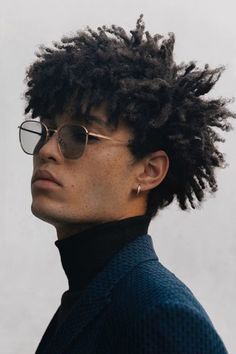 a man with dreadlocks wearing sunglasses and a turtle neck sweater looks off to the side