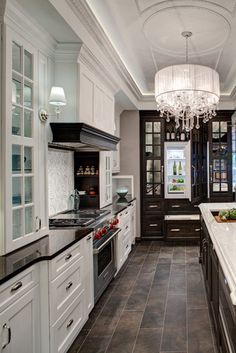 a large kitchen with white cabinets and black counter tops, along with a chandelier hanging from the ceiling