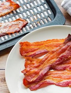 bacon strips on a white plate next to a grill