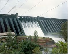 a large dam with water coming out of it's sides and power lines above