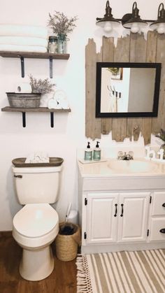 a white toilet sitting next to a sink in a bathroom under a wooden framed mirror