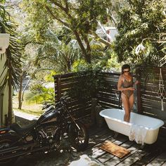 a woman in a bathing suit standing next to a white bathtub and black motorcycle