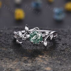 a close up view of a ring with leaves and green stone in the center on a rock