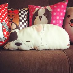 four pillows with dogs on them are sitting on a brown couch, one is white and the other has pink polka dots