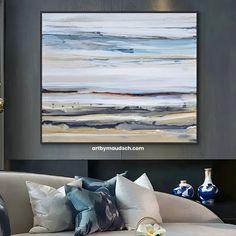 an abstract painting hangs on the wall above a couch with decorative pillows and vases