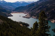 a large body of water surrounded by mountains and pine trees in the foreground is a lake