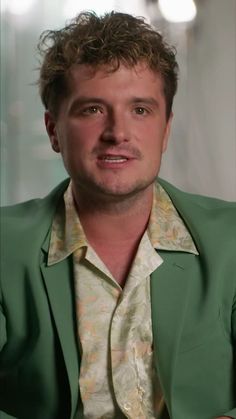 a man in a green jacket and floral shirt is looking at the camera with an intense look on his face