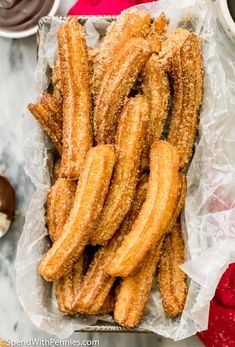 fried churros in a basket with dipping sauce on the side