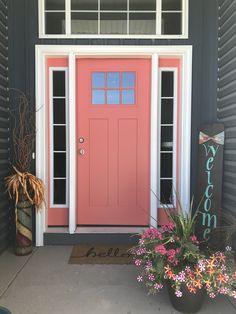 a pink front door with two potted plants next to it and a welcome sign