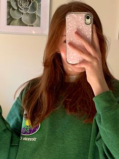 a woman taking a selfie in front of her cell phone while wearing a green sweatshirt