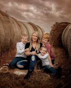 a woman and two boys sitting on hay bales with their arms around each other