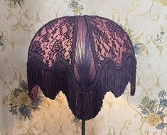 a pink and purple lace hat on a wooden stand in front of a wallpapered background