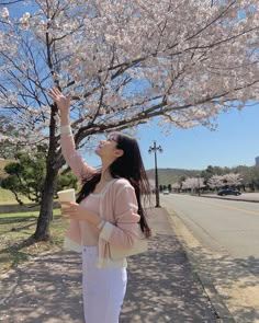 a woman standing under a tree with her arms in the air while holding a cup