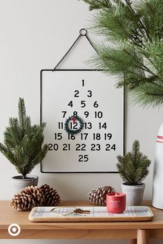 a wooden table topped with pine cones and plants next to a white wall mounted calendar