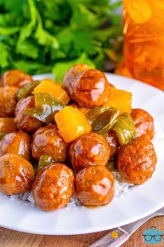 a white plate topped with meatballs covered in sauce and vegetables next to a glass of orange juice