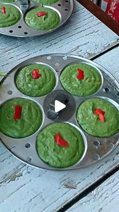 cupcakes with green icing and red pepper on them sitting in a muffin tin