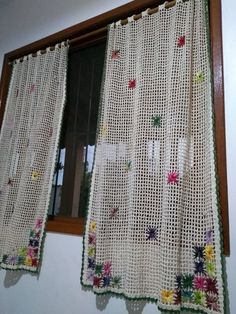 the curtain is made from crochet and has colorful flowers on it, along with a brown wooden window frame