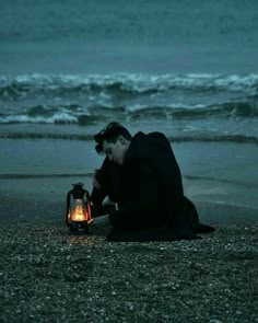 a man kneeling down next to a lantern on the beach