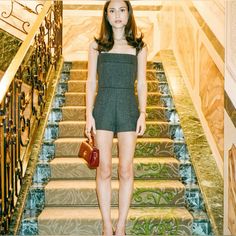 a woman standing in front of some stairs holding a handbag and wearing high heels