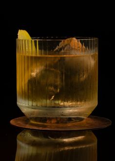 a glass filled with liquid sitting on top of a wooden plate next to a black background