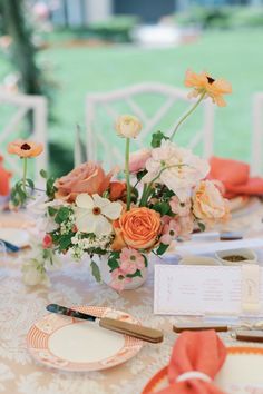 an arrangement of flowers in a vase on a table with place cards and napkins